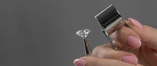 Close up of a woman's hand holding a loupe inspecting a real lab grown diamond held in the other hand