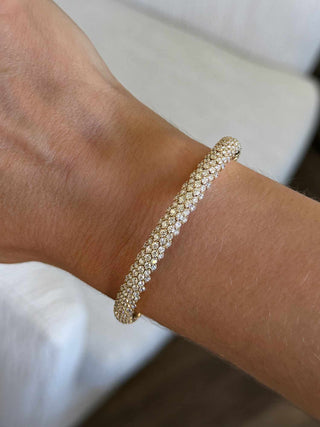 Close-up of a woman's wrist wearing a lab grown diamond stretch bangle bracelet in yellow gold, inside with soft light. 