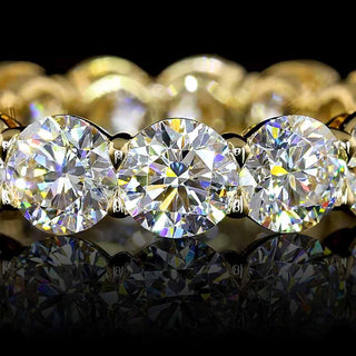 Close up of round lab grown diamond eternity band in 14k yellow gold, with shared claw prongs and open basket setting.