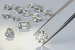 Round diamond held by diamond tweezers, with loose diamonds in the background.