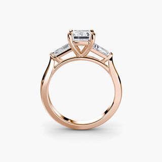 Three stone engagement ring setting in rose gold, side profile view with an emerald-cut lab grown center diamond and tapered baguette side stones. || #metal_rose gold #diamond shape_emerald