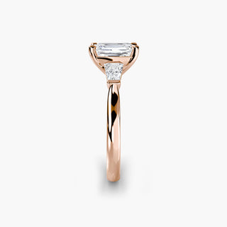Three stone engagement ring setting in rose gold showing the band profile, with an emerald-cut lab grown center diamond and tapered baguette side stones. || #metal_rose gold #diamond shape_emerald