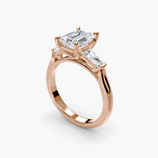 Three stone engagement ring setting in rose gold with an emerald-cut lab grown center diamond and tapered baguette side stones, three-quarter view. || #metal_rose gold #diamond shape_emerald