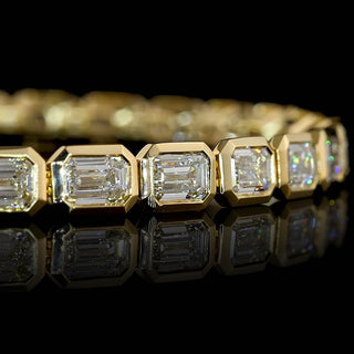Close-up of East-West Emerald-cut lab grown diamond tennis bracelet in 14k yellow gold bezel setting.